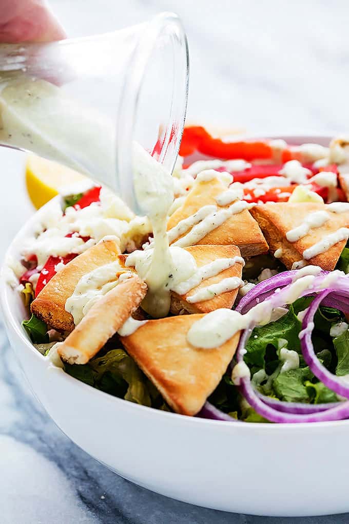 tzatziki dressing being poured on top of chicken gyro salad in a bowl.