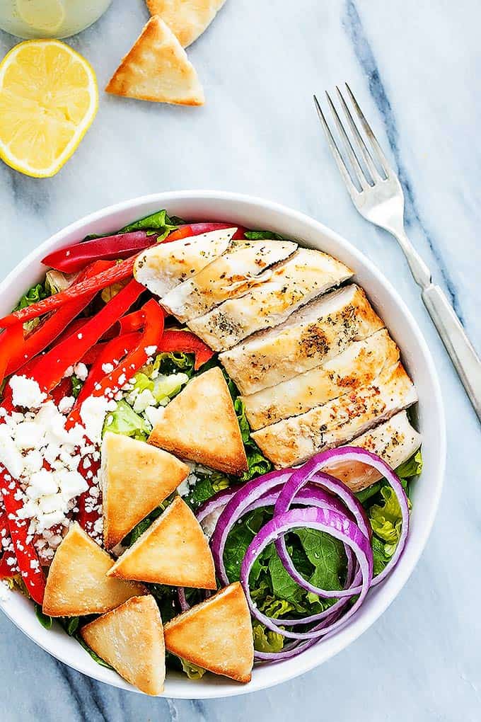 top view of chicken gyro salad with tzatziki dressing in a bowl with a half of a lemon, pita croutons and a fork on the side.