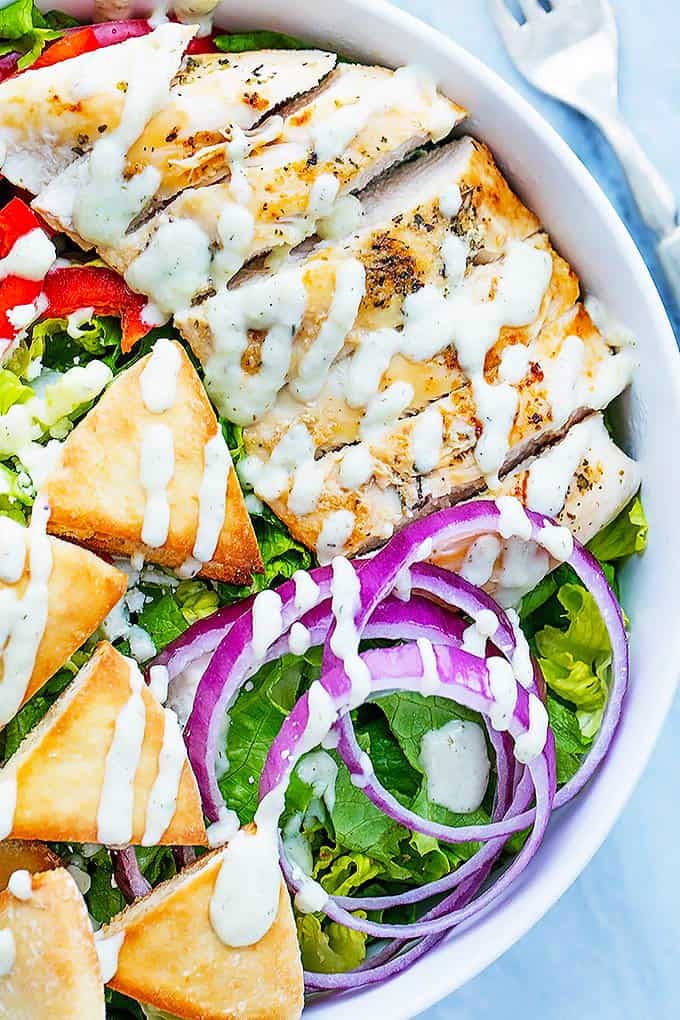 close up of chicken gyro salad with tzatziki dressing in a bowl with a fork on the side.