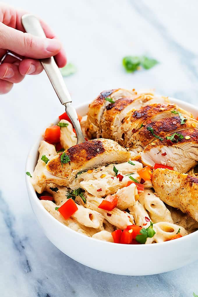 a hand holding a fork grabbing some Chili's cajun alfredo pasta from a bowl.