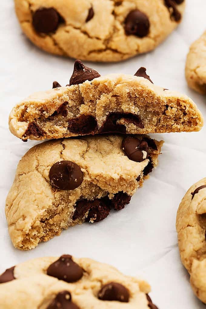 a coconut oil cream cheese chocolate chip cookie broken in half with one half laying on top of the other with. more cookies around it.