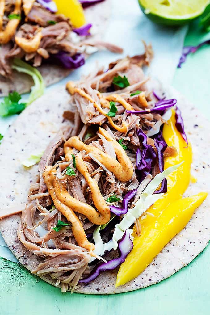 an open kalua pork taco with another taco and lime halve in the background.