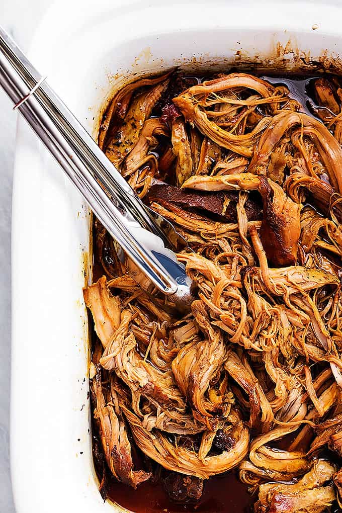 close up of slow cooker honey balsamic pork tenderloin and tongs in a baking pan.