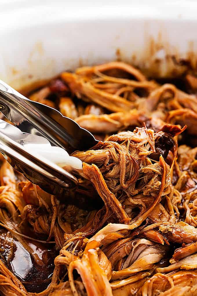 close up of tongs picking up some slow cooker honey balsamic pork tenderloin from a baking pan.