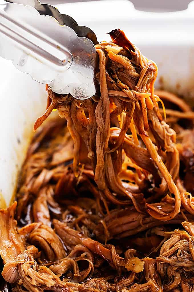 close up of tongs picking up some slow cooker honey balsamic pork tenderloin from a pan.