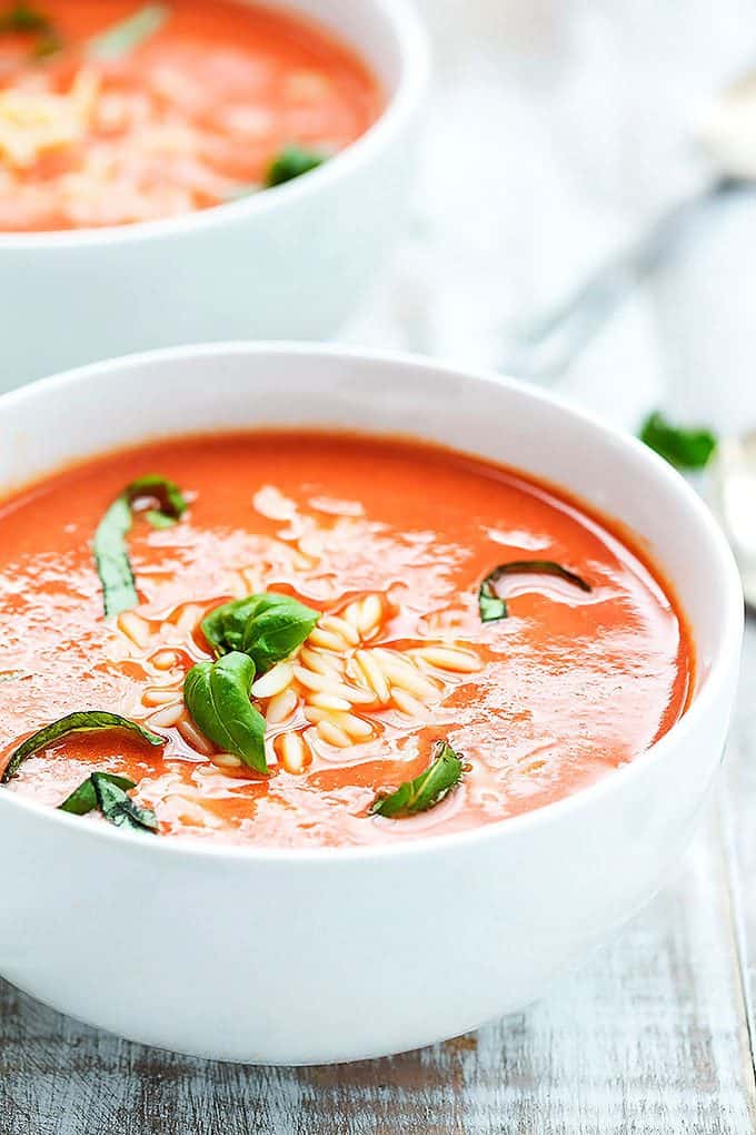 tomato basil orzo soup in a bowl with a spoon and another bowl of soup in the background.