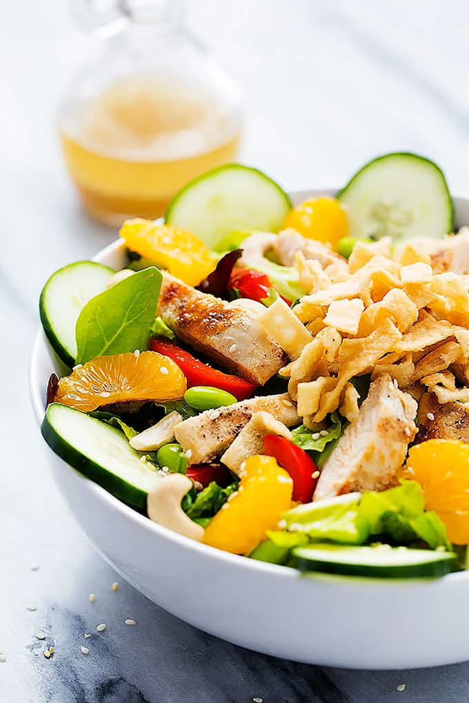 Asian citrus chicken salad in a bowl with sesame ginger dressing in a carafe in the background.