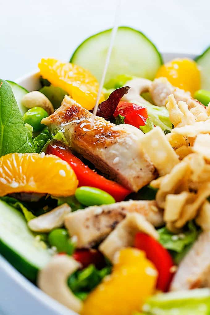 close up of Asian citrus chicken salad in a bowl with sesame ginger dressing being poured on top.