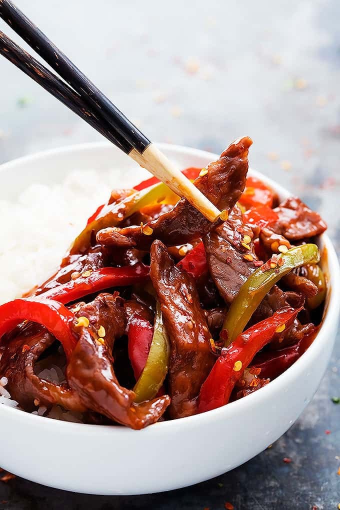 chopsticks picking up some Beijing beef from a bowl of beef and rice.