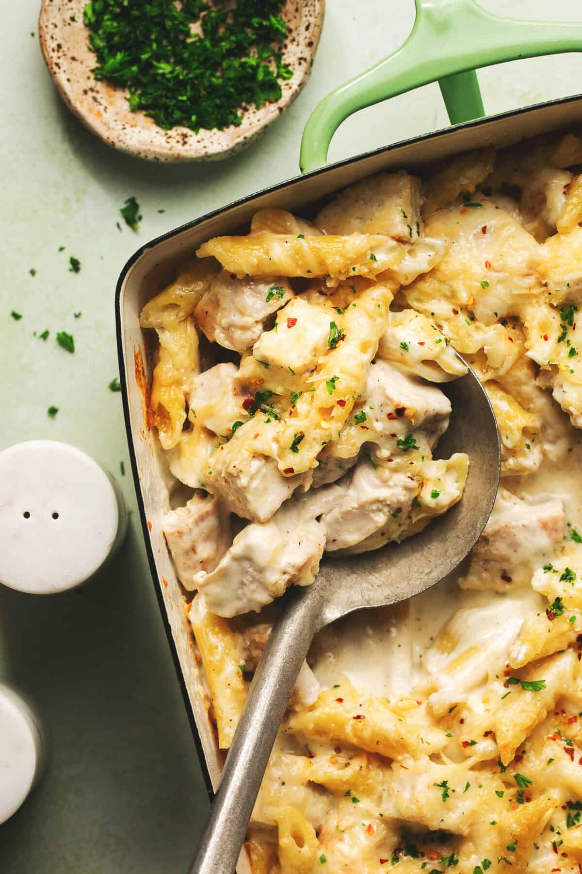 spoon scooping into casserole dish with chicken and pasta