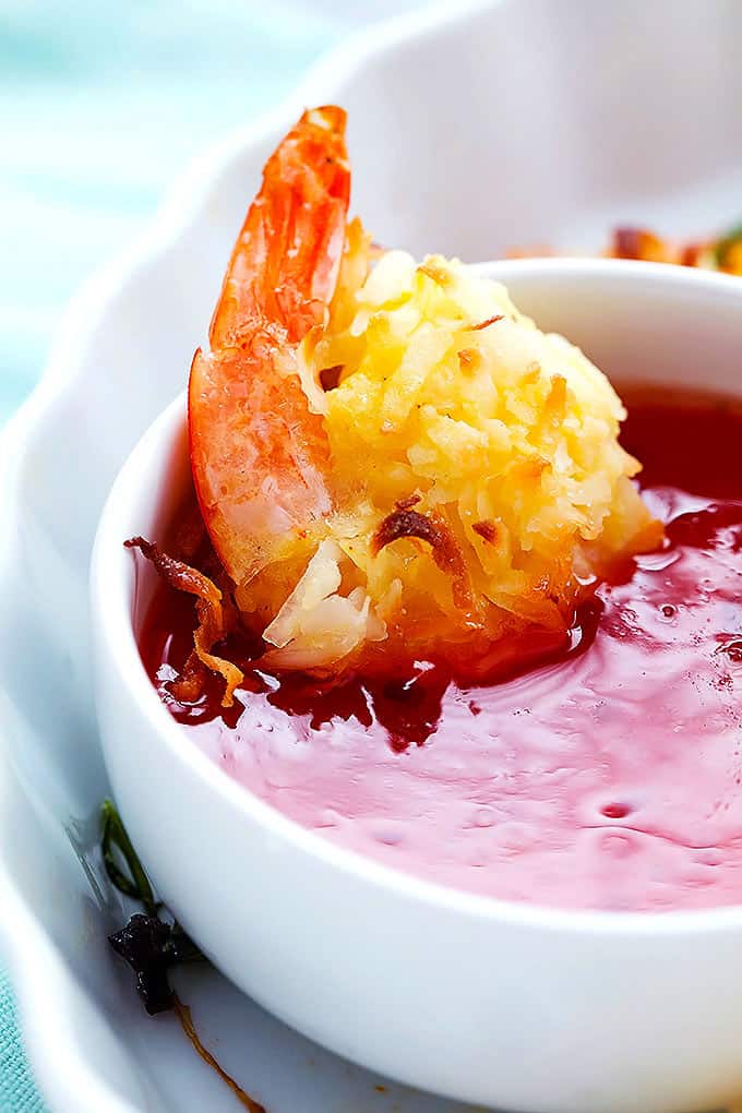 close up of a baked coconut shrimp dipped in a bowl of sweet and sour sauce.