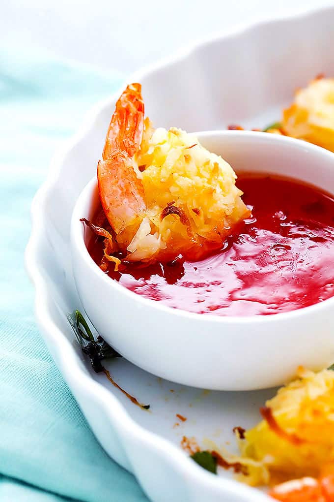 a baked coconut shrimp dipped in a bowl of sweet and sour sauce.