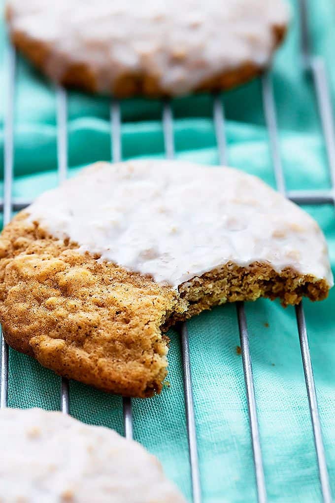 a half iced oatmeal cookie with a bite missing on a cooling rack with more cookies around it.