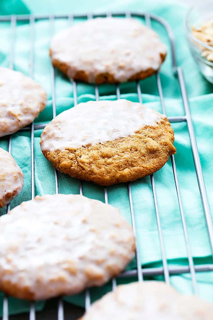iced oatmeal cookies on a cooling rack with one cookie half iced.