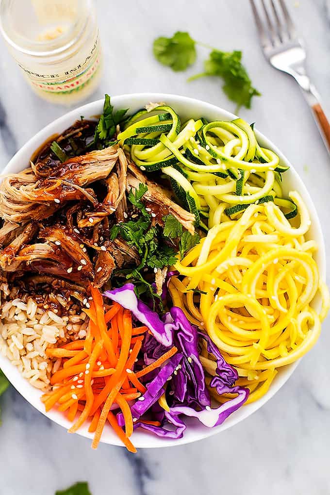  top view of a slow cooker luau pork rice bowl with a container of sesame seeds and a fork on the side.