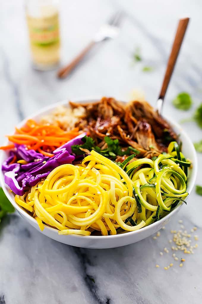 a slow cooker luau pork rice bowl with a fork in the bowl with a container of sesame seeds and another fork in the background.