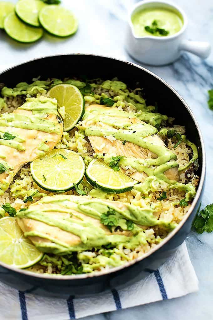 one pot cilantro lime chicken & rice with wheels of lime and creamy avocado sauce in the background.