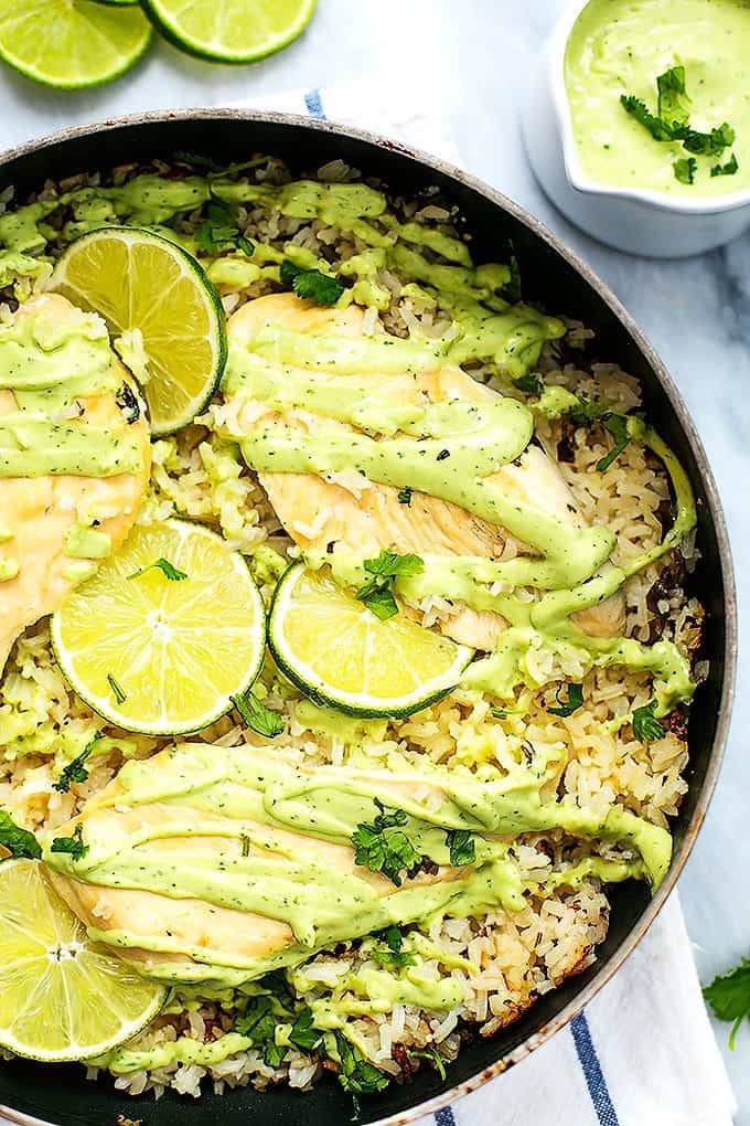 top view of one pot cilantro lime chicken & rice with wheels of lime and creamy avocado sauce on the side.