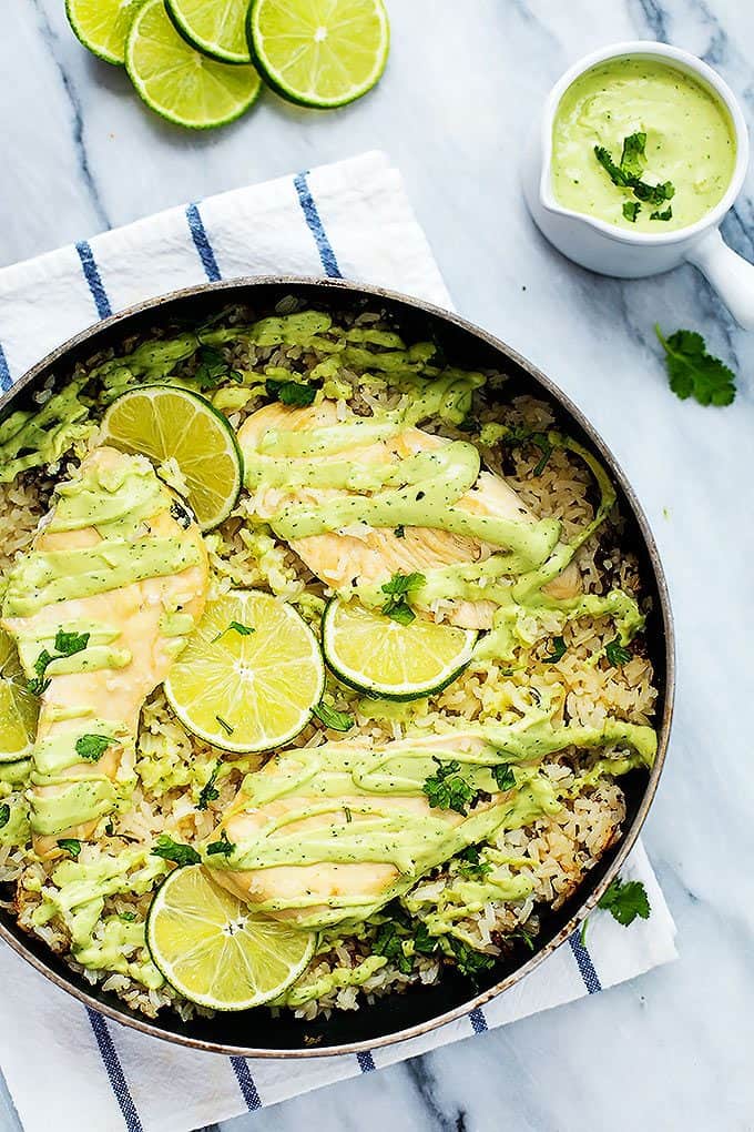 top view of one pot cilantro lime chicken & rice with wheels of lime and creamy avocado sauce on the side.