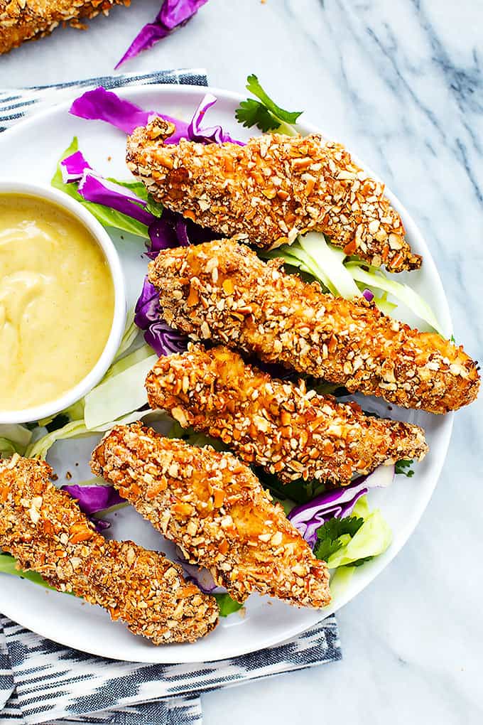 top view of baked pretzel crusted chicken tenders with dipping sauce on a plate.