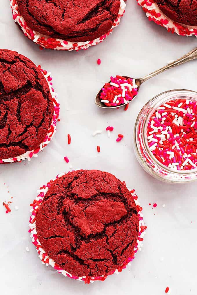 top view of red velvet sandwich cookies with a jar of sprinkles and a spoon with sprinkles on top.