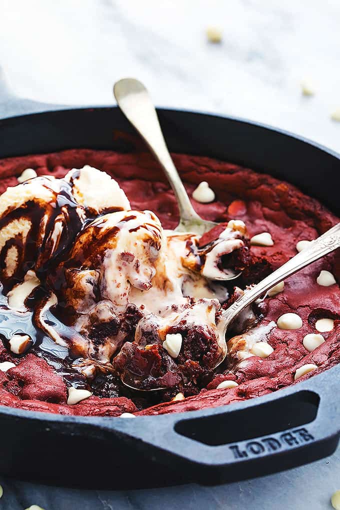 red velvet skillet cookie topped with vanilla ice cream and chocolate sauce with spoons with bites on them laying on top.