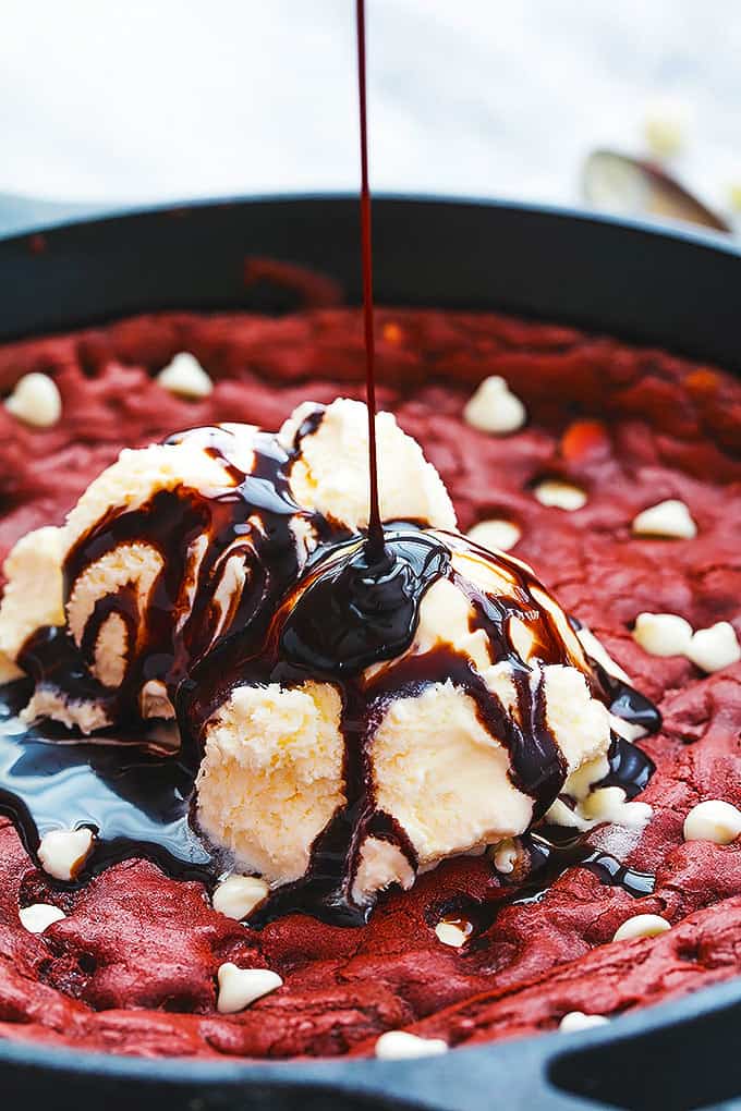 red velvet skillet cookie topped with vanilla ice cream with chocolate sauce being poured on top.
