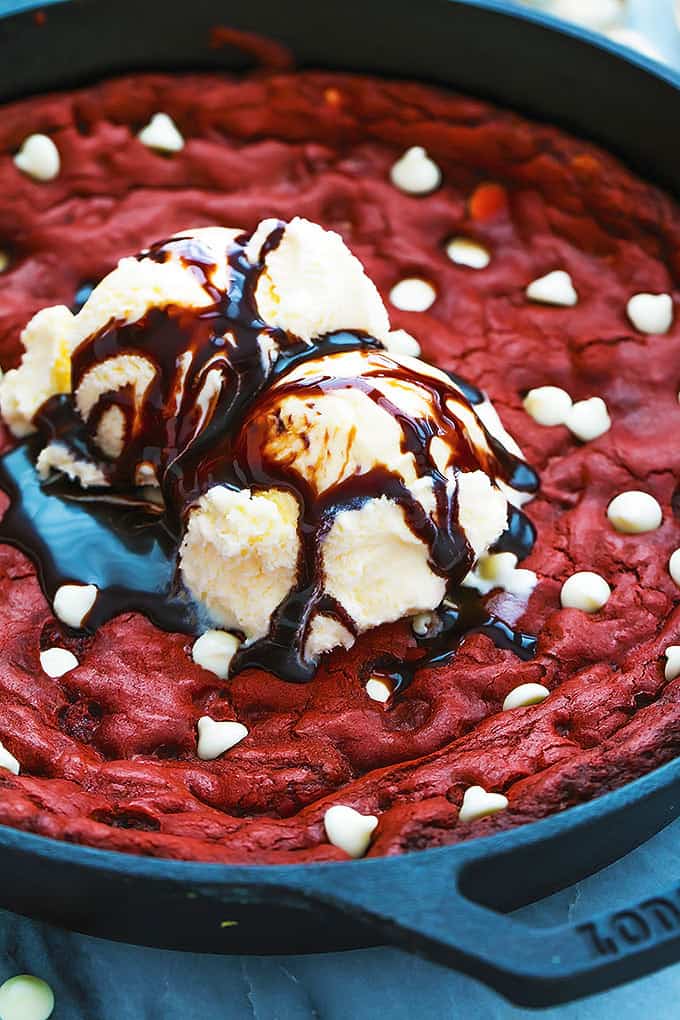 close up of a red velvet skillet cookie topped with vanilla ice cream and chocolate sauce.
