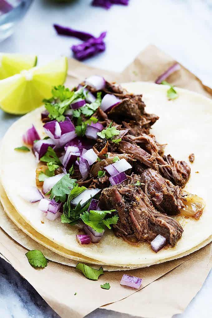 slow cooker barbacoa beef on a stack of tortillas with lime slices on the side.