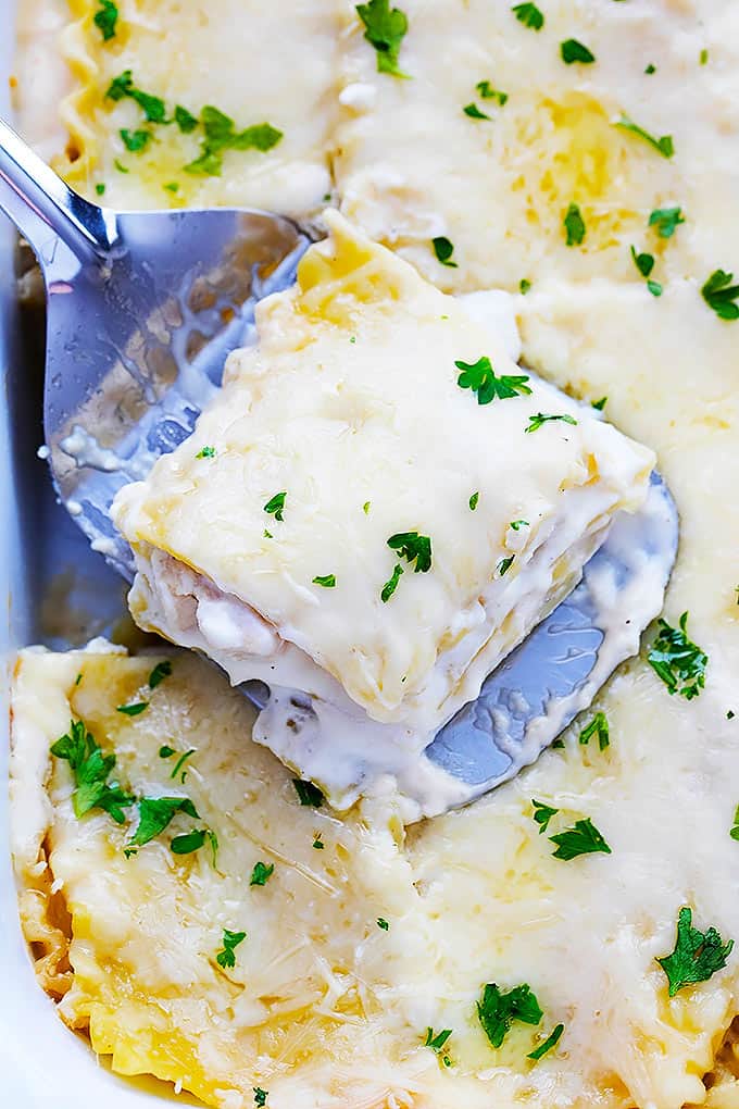 close up top view of a spatula holding a piece of slow cooker three cheese chicken lasagna on the rest of the lasagna.