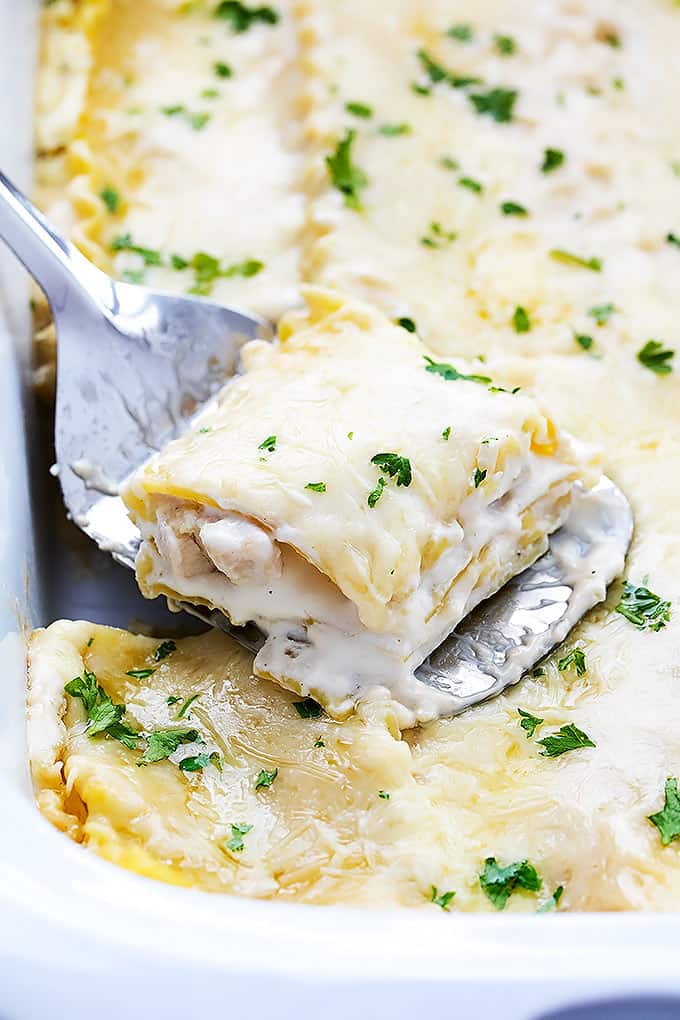 close up of a spatula holding a piece of slow cooker three cheese chicken lasagna on top of the rest of the lasagna in a serving tray.