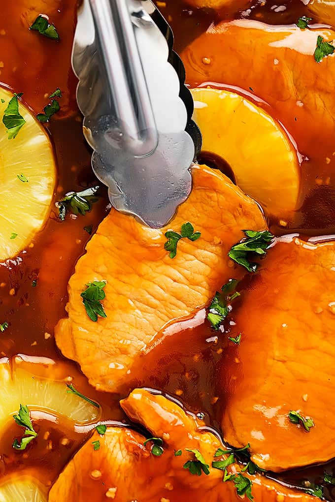 close up of tongs grabbing some slow cooker Hawaiian pork chops.