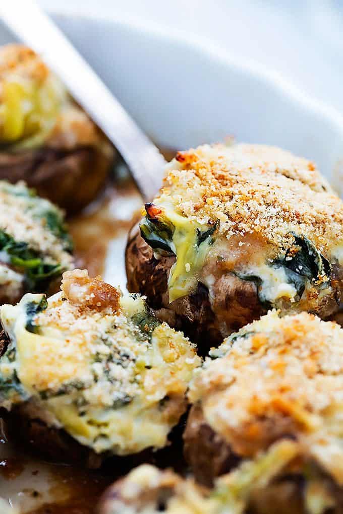 close up of a spinach artichoke dip stuffed mushroom on a fork with more mushrooms around it.