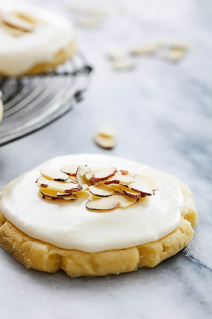 an almond sugar cookie topped with almond cream cheese frosting and almond shavings.