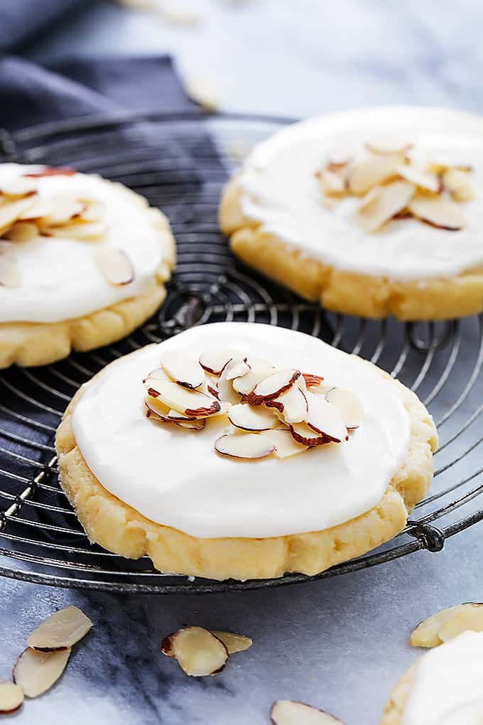 almond sugar cookies on a round cooling rack topped with almond cream cheese frosting and almond shavings.
