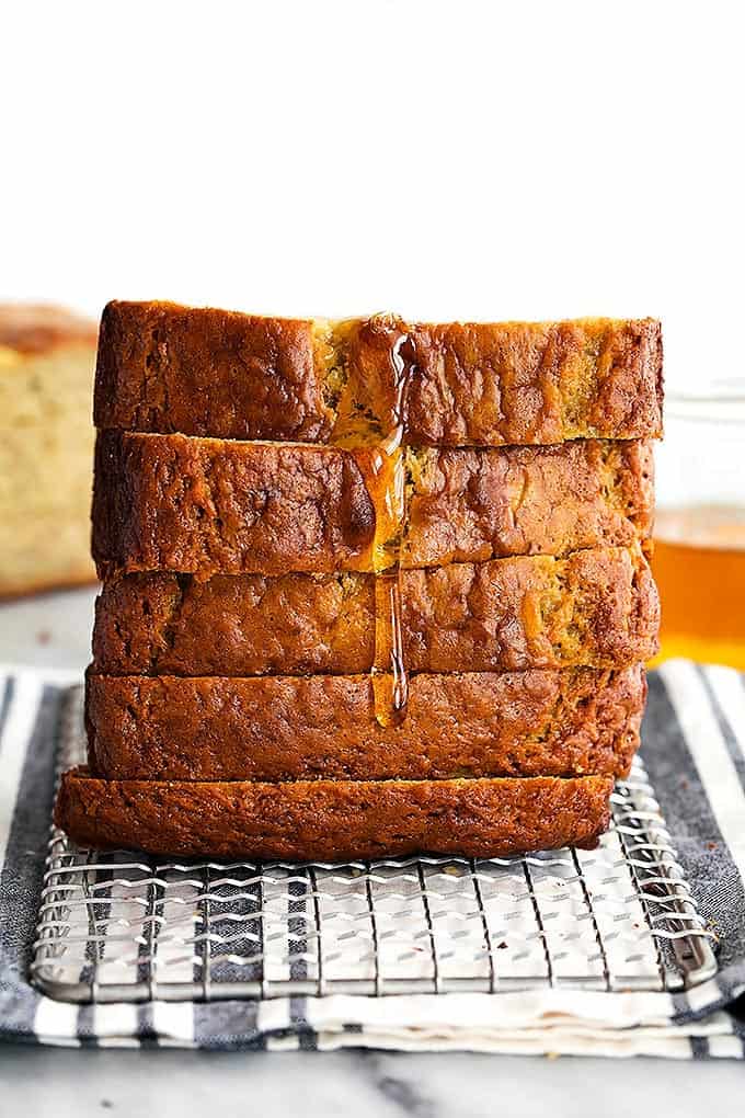 stacked slices of brown butter banana bread on a cooling rack with honey dripping down the side.