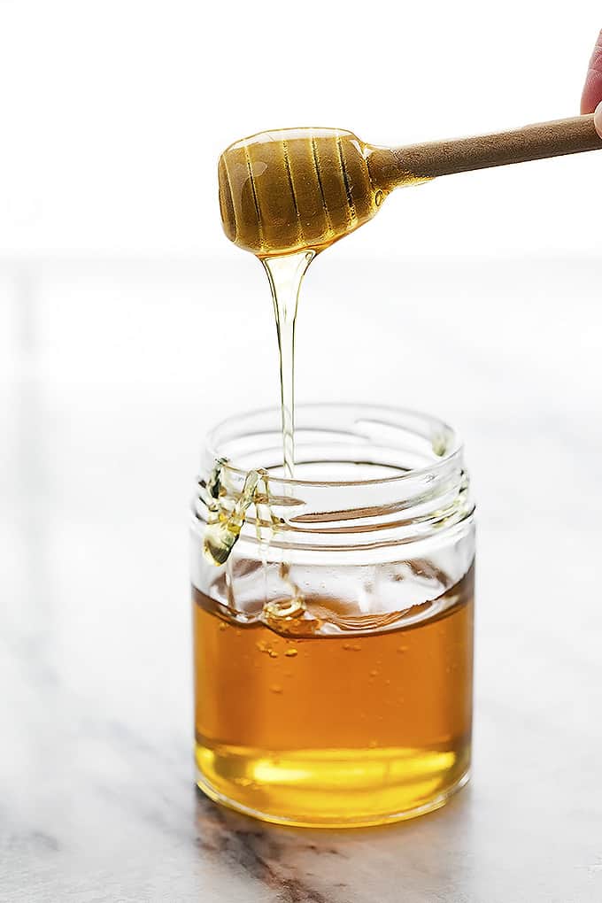 a honey dipper with honey on top being held above a jar of honey.