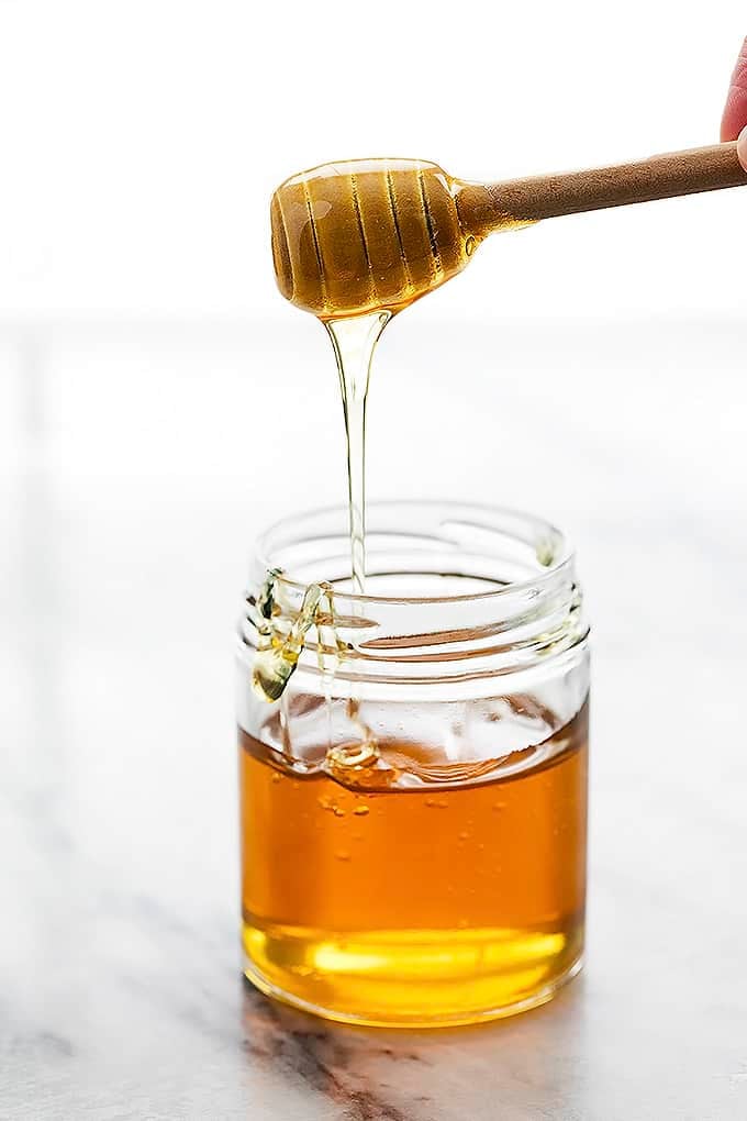 a honey dipper with honey on top being held above a jar of honey.