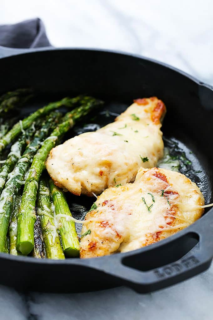 close up of garlic parmesan chicken & asparagus in a cast iron skillet.