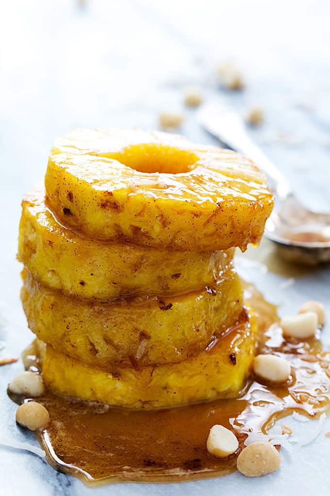 stacked caramelized pineapples on top of pan sauce and macadamia nuts with a spoon on the side.
