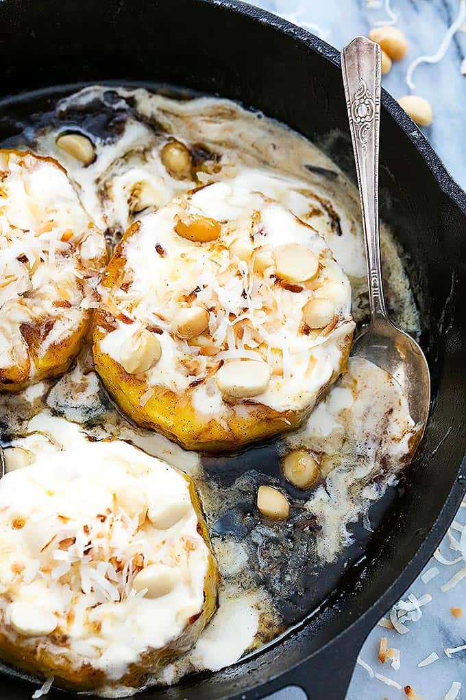 top view of caramelized pineapple sundaes topped with ice cream, macadamia nuts, and coconut shavings with a spoon on the side all on a cast iron.