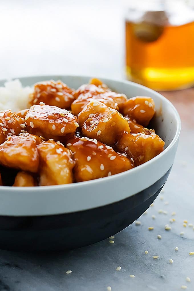 slow cooker honey sesame chicken with rice in a bowl with a jar of honey faded in the background.