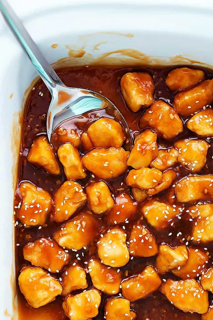 close up top view of slow cooker honey sesame chicken with a serving spoon in a serving pan.
