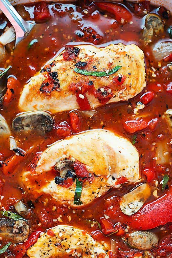 close up of slow cooker Tuscan chicken and a serving spoon.
