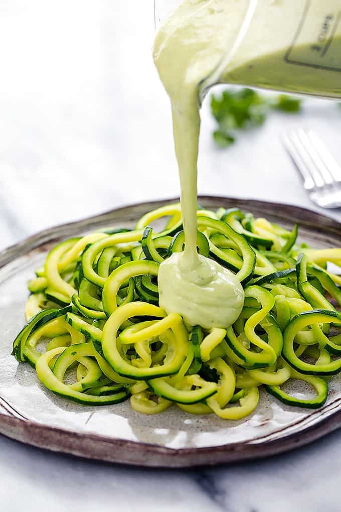 cilantro lime avocado sauce being poured on top of zoodles on a plate.