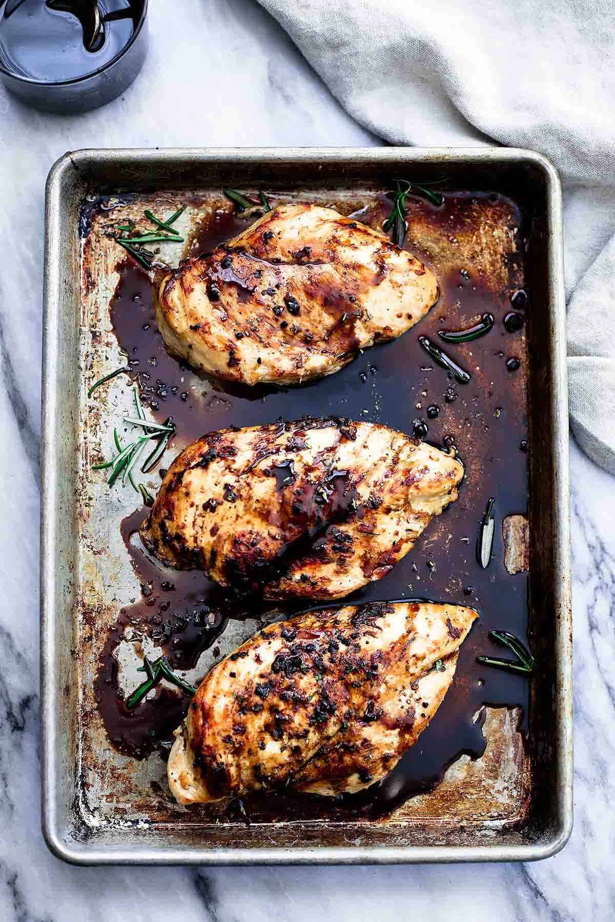 top view of baked balsamic chicken in a baking sheet with a glass of balsamic vinegar on the side.