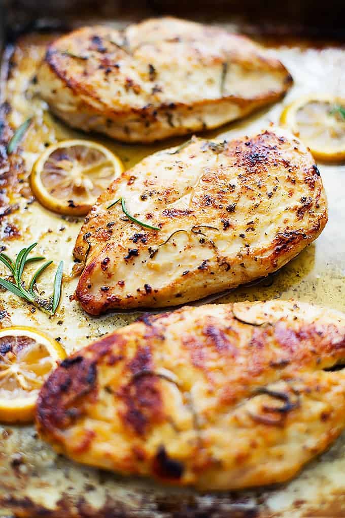 close up of healthy baked lemon chicken in a baking sheet.
