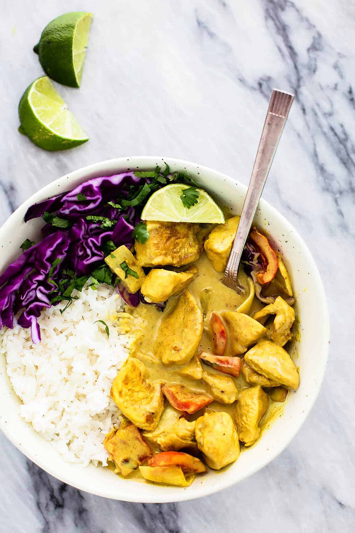 top view of coconut curry chicken with rice and a fork in a bowl with lime slices on the side.