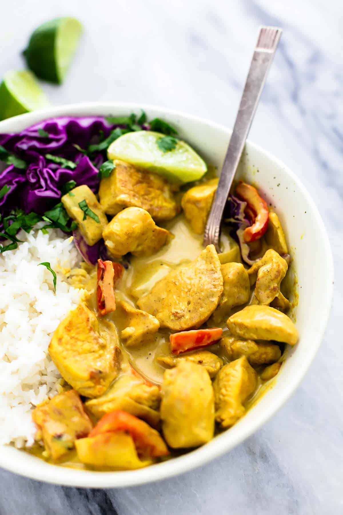 coconut curry chicken with rice and a spoon in a bowl with slices of limes on the side.