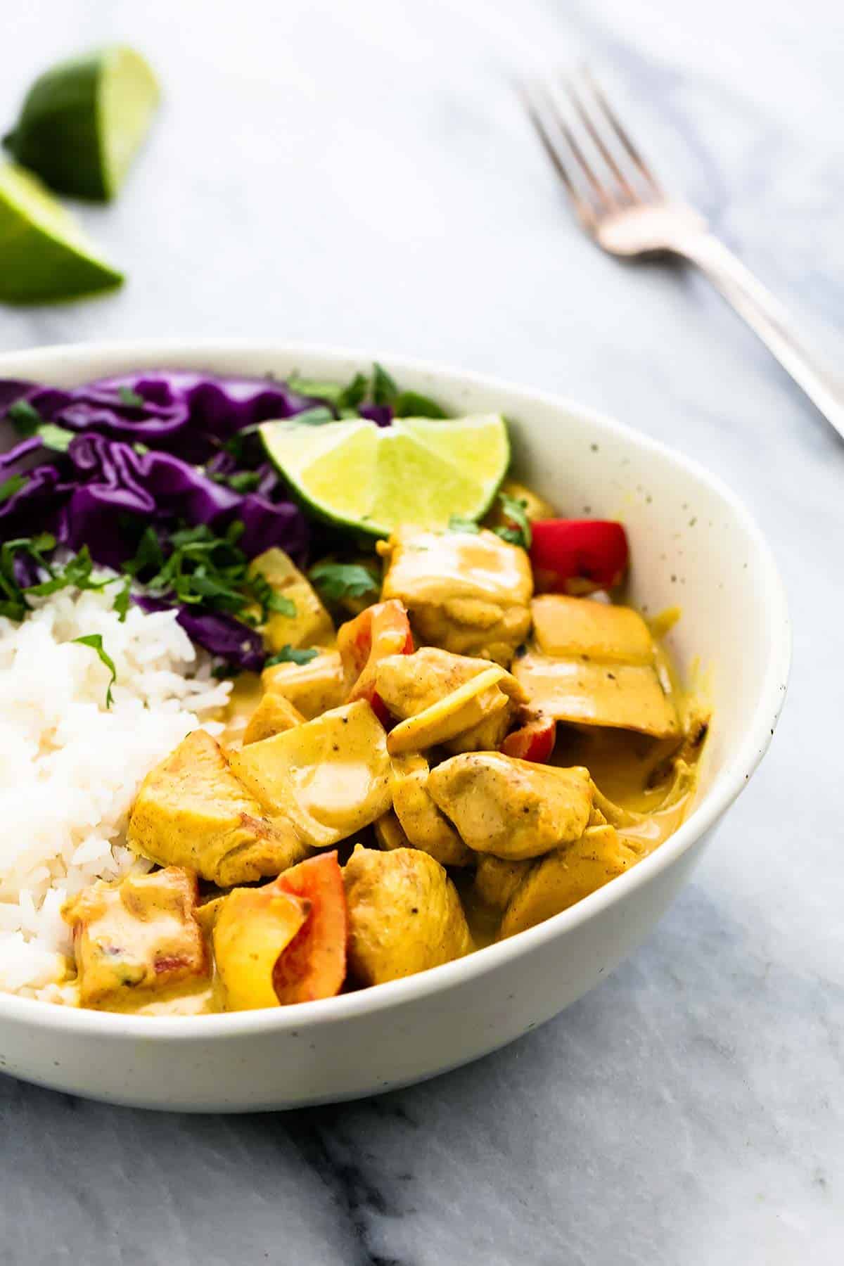 coconut curry chicken with rice in a bowl with lime slices and a fork in the background.